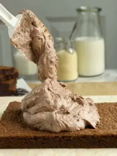 a spatula piling malted chocolate frosting onto a brownie