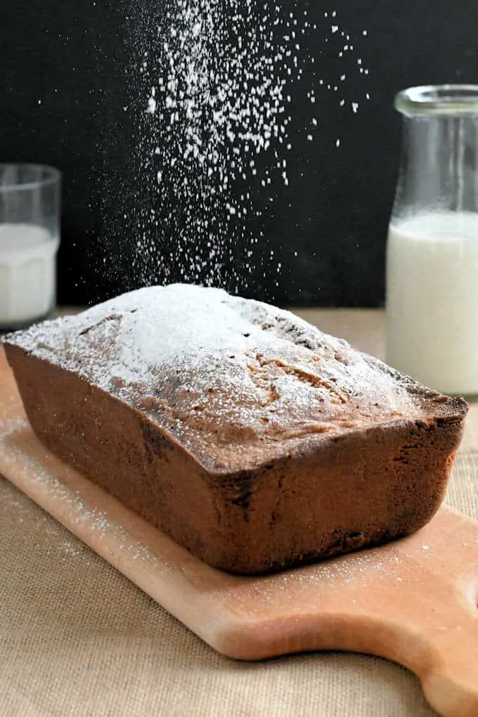 a whole pound cake on a board with sprinkles of powdered sugar cascading on the cake