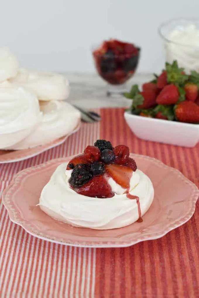 a pavlova on a pink plate topped with ceam and berries.