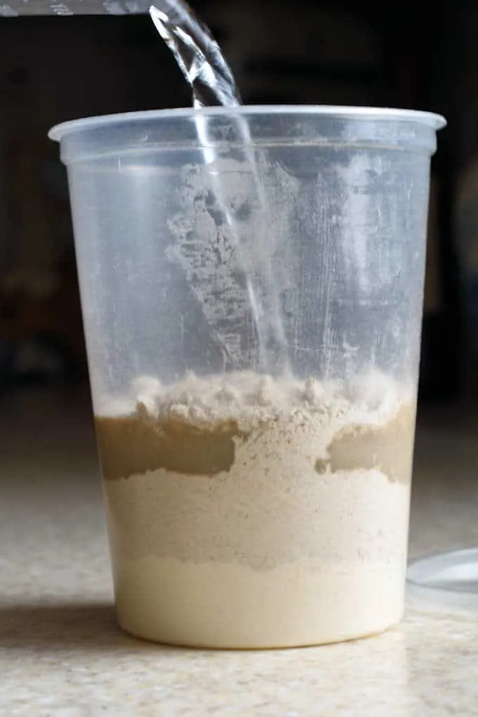 a plastic deli container with flour and water being mixed for sourdough starter