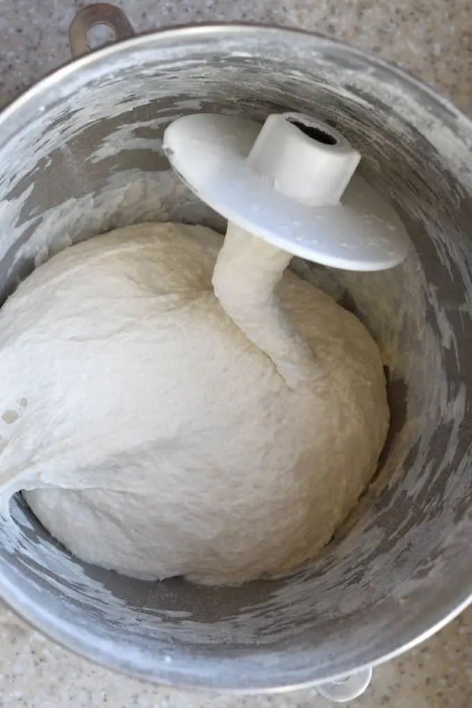 a mixing bowl filled with sourdough bread dough and a dough hook.