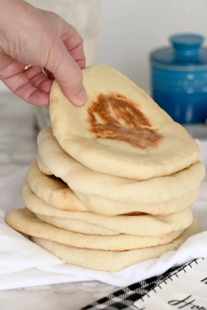 a hand grabbing a pita bread from a stack