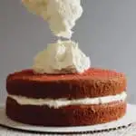 a spatula dropping ermine frosting onto a red velvet cake
