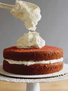 a spatula dropping ermine frosting onto a red velvet cake