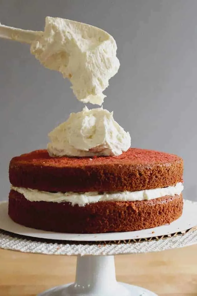 a spatula dropping ermine frosting onto a red velvet cake