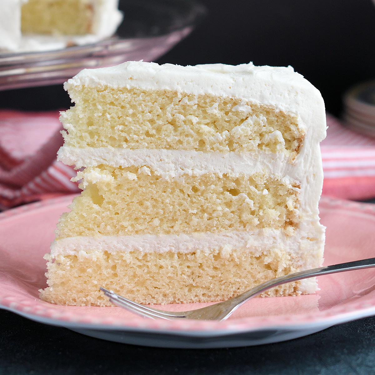 a slice of vanilla buttermilk cake standing on a pink plate with a fork.