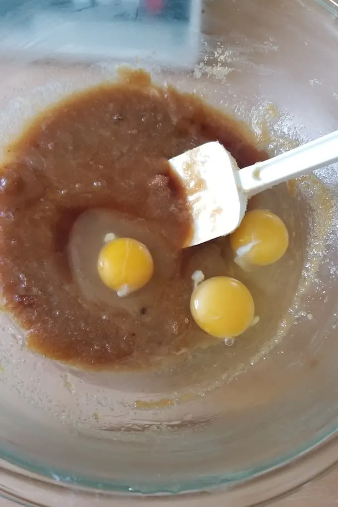 a bowl of butter and brown sugar with eggs added.