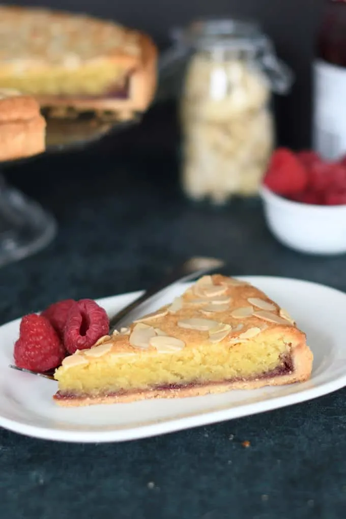 a slice of bakewell tart on a white plate with raspberries