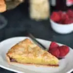 a slice of bakewell tart in a plate with a fork and raspberries