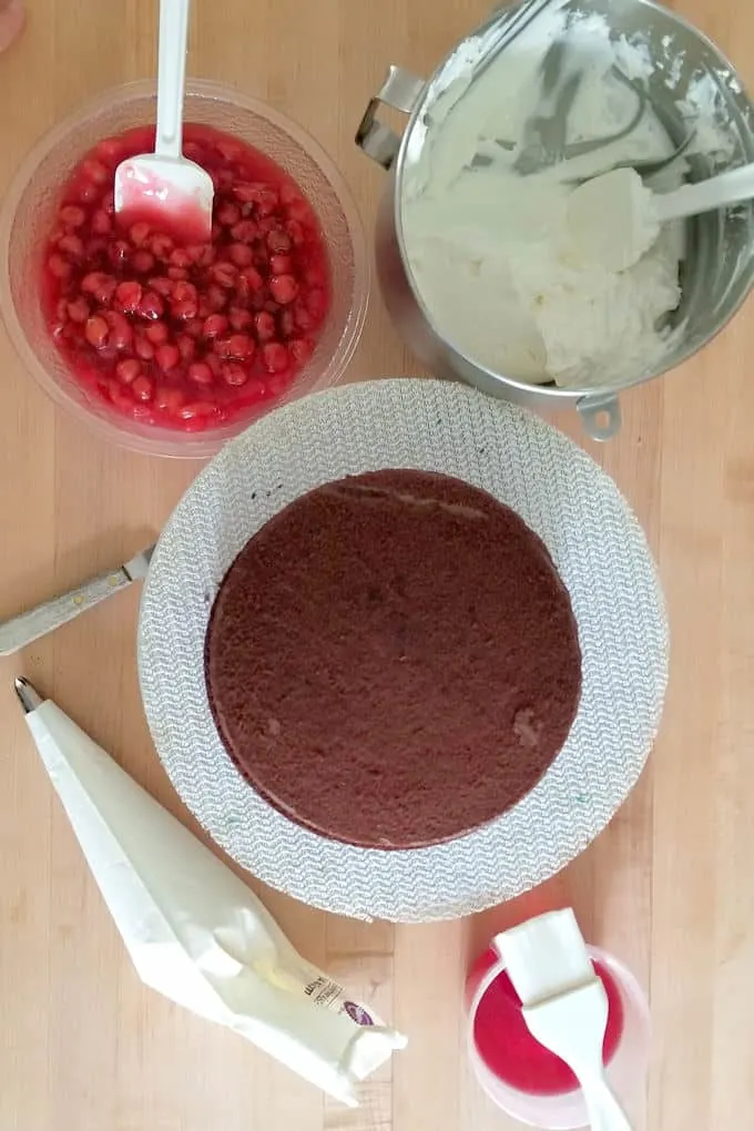 Cherries, whipped cream, kirschwasser syrup and chocolate cake assembled on a table.