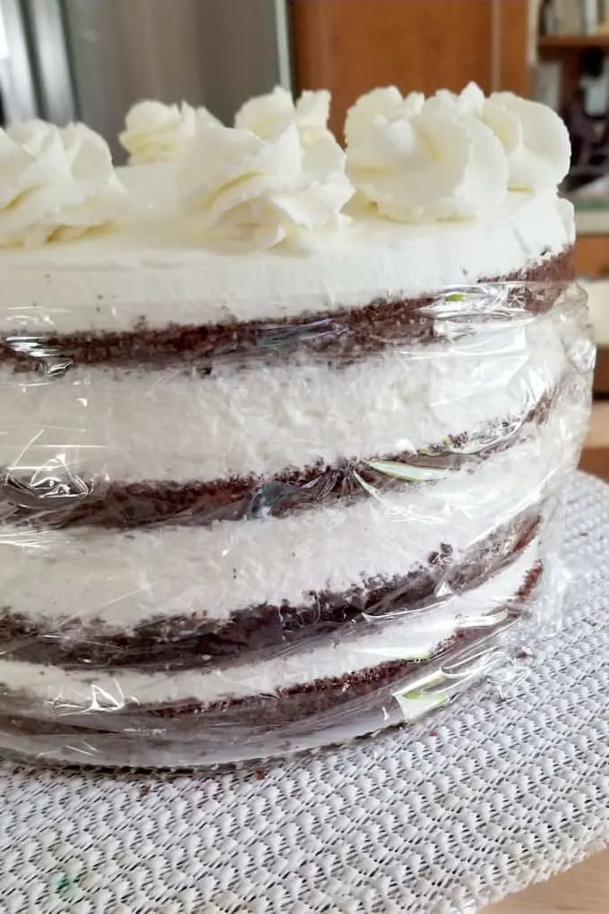 showing how to wrap the sides of a black forest cake with plastic to prevent it from drying out.