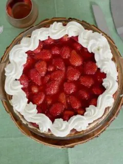 a fresh strawberry pie with whipped cream on a green tablecloth.