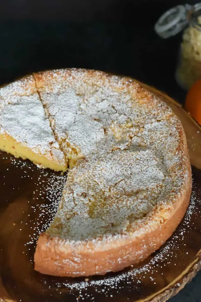 a partially slice flourless almond cake on a wood cake stand