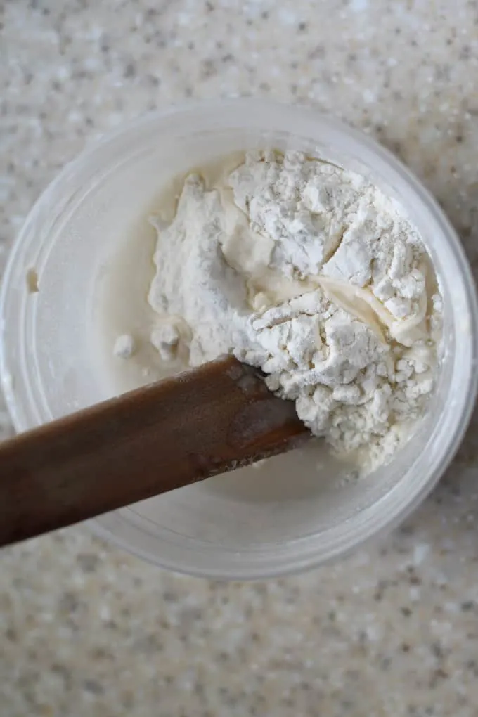 a plastic container with rehydrated sourdough starter and flour being mixed in