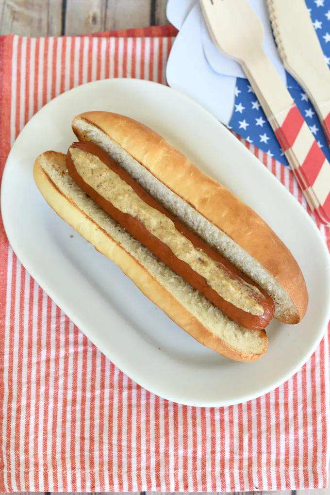 a hot dog with mustard on a homemade bun with red, white & blue table setting