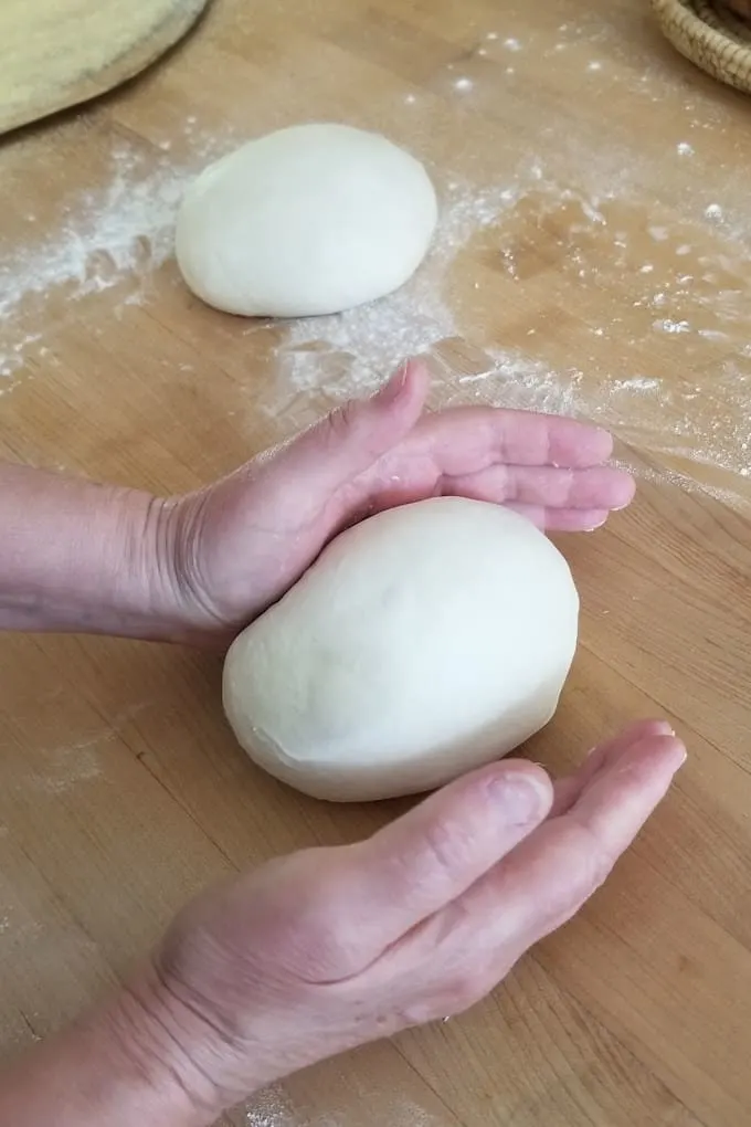 two hands pushing pizza dough back and forth to form a tight ball.