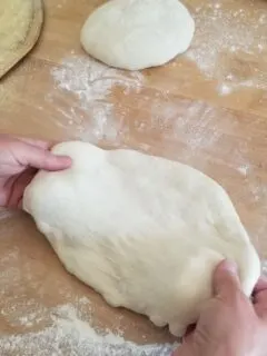 two hands pulling on pizza dough to stretch