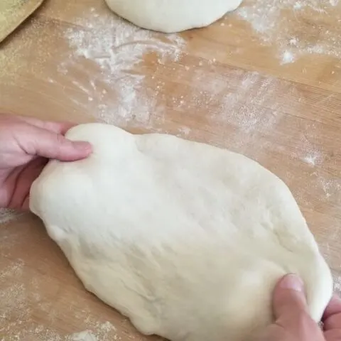 two hands pulling on pizza dough to stretch