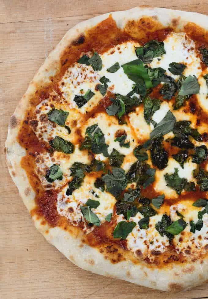 A closeup shot of a pizza made with sourdough crust. The pizza is on a cutting board.
