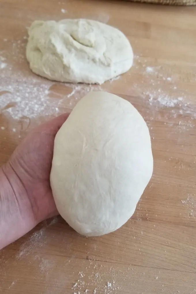 a hand pulling in the sides of a piece of dough to form a ball