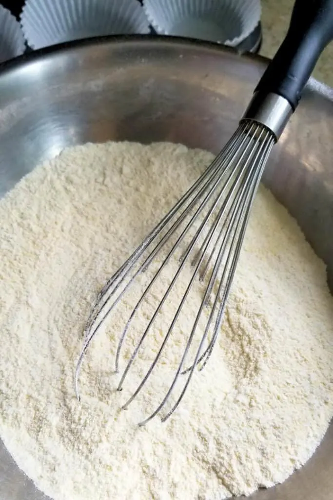 a bowl of dry ingredients for cornbread muffins with a whisk in the bowl