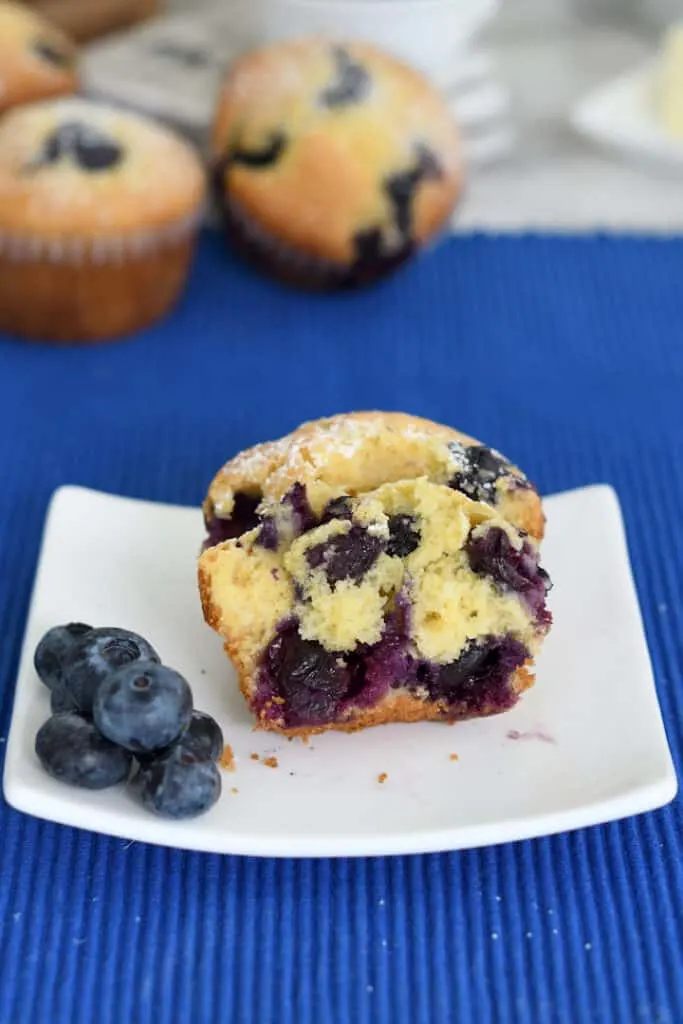 a blueberry cornbread muffin cut in half to show the inside. It's on a white plate with a few fresh berries