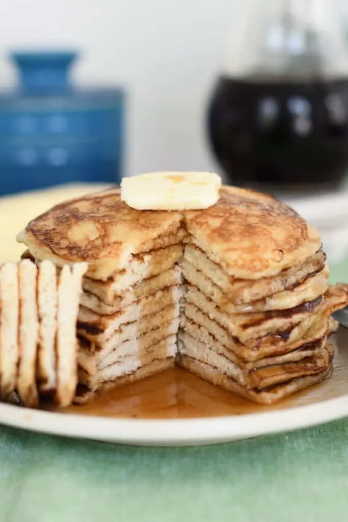 a stack of sourdough pancakes with a wedge cut out to show the middle of the pancakes. A pat of butter on top and syrup on the plate