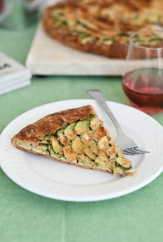 a slice of zucchini galette on a white plate with a glass of rose wine