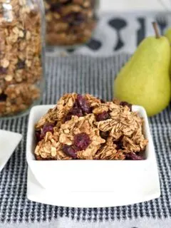 an image of a bowl of chunky granola on a table with fruit and honey