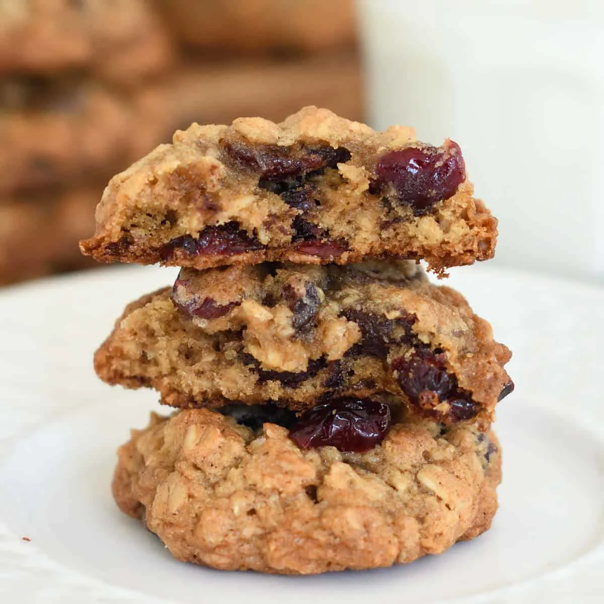 a stack of oatmeal cranberry chocolate chip cookies on a plate. One cookie is split to show the inside