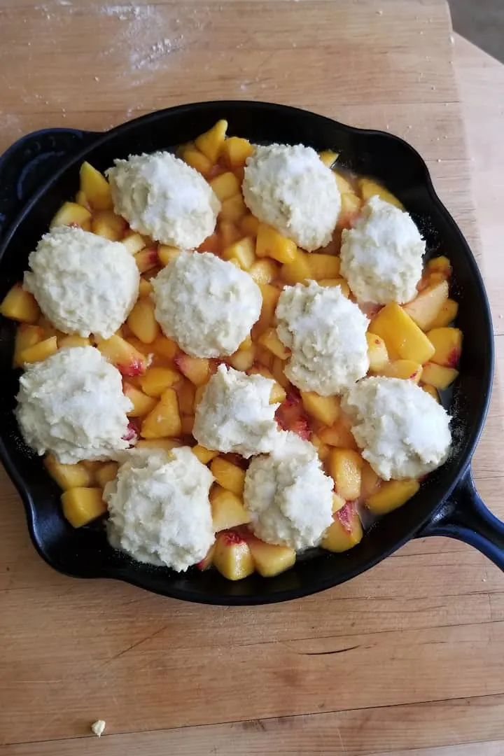 peach in a skillet topped with unaked biscuit dough.