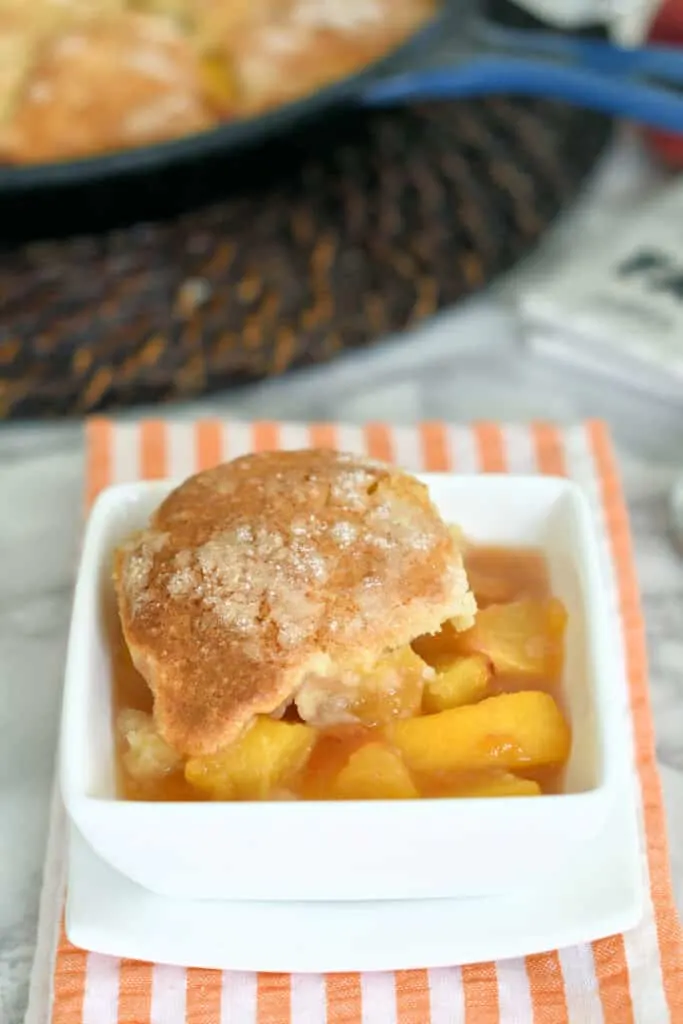 Peache cobbler with a cream biscuit in a white bowl.