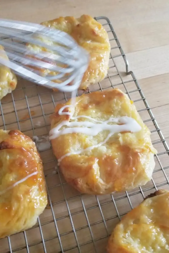 cheese danish on a cooling rack being glazed