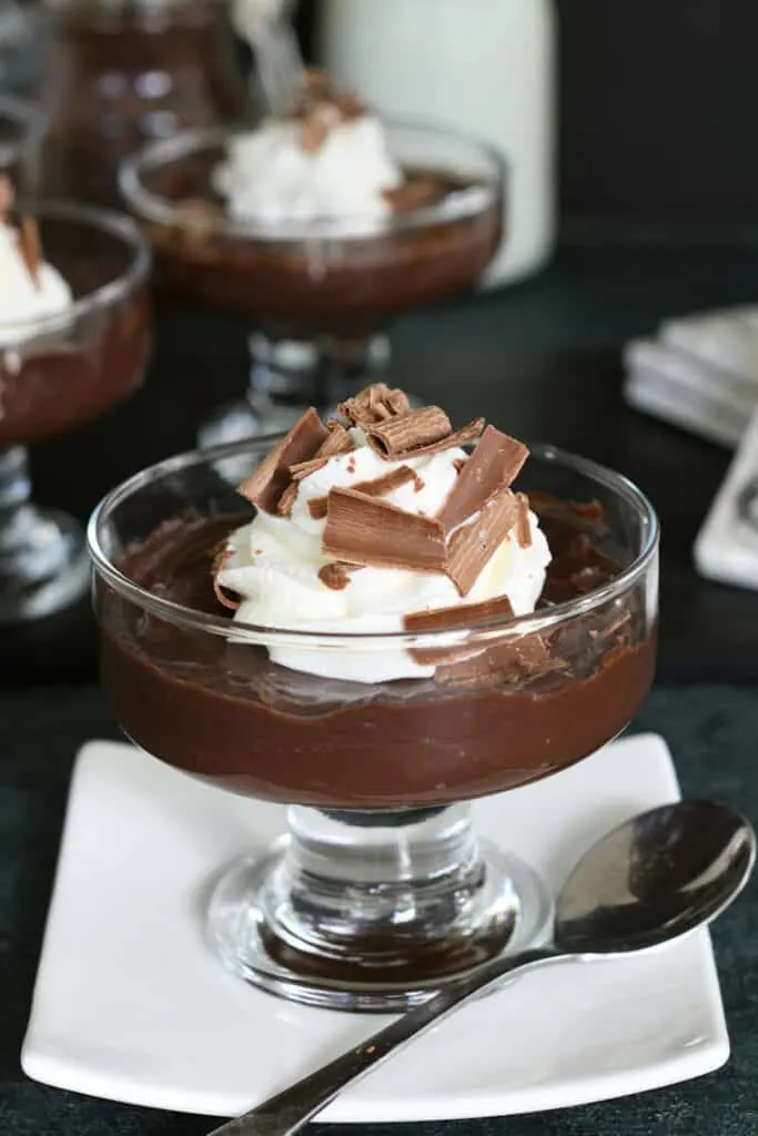 a dessert dish filled with dark chocolate pudding with whipped cream and chocolate shavings.