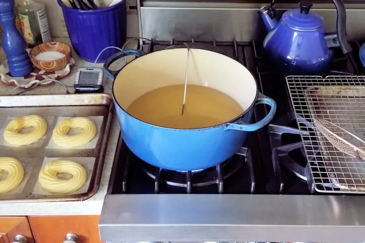 a photo showing the setup for frying french crullers. Batter, oil and draining rack lined up.
