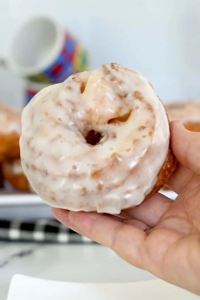 a hand holding a large, glazed french cruller