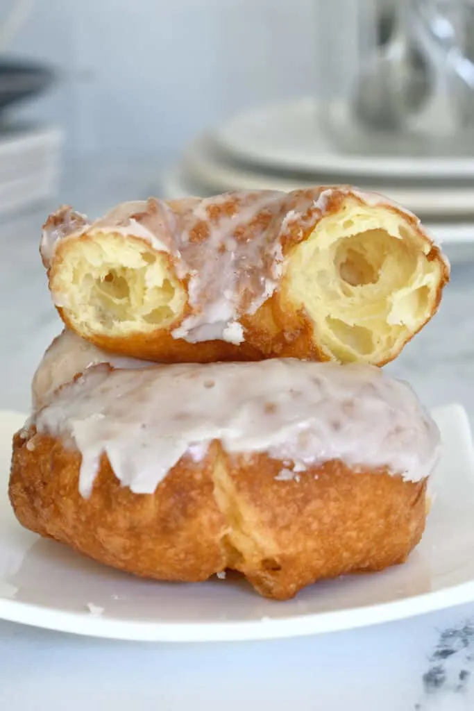 a french cruller on a plate with a broken cruller on top showing the open interior crumb