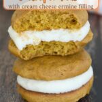 two pumpkin whoopie pies on a wood table. one with a bite.