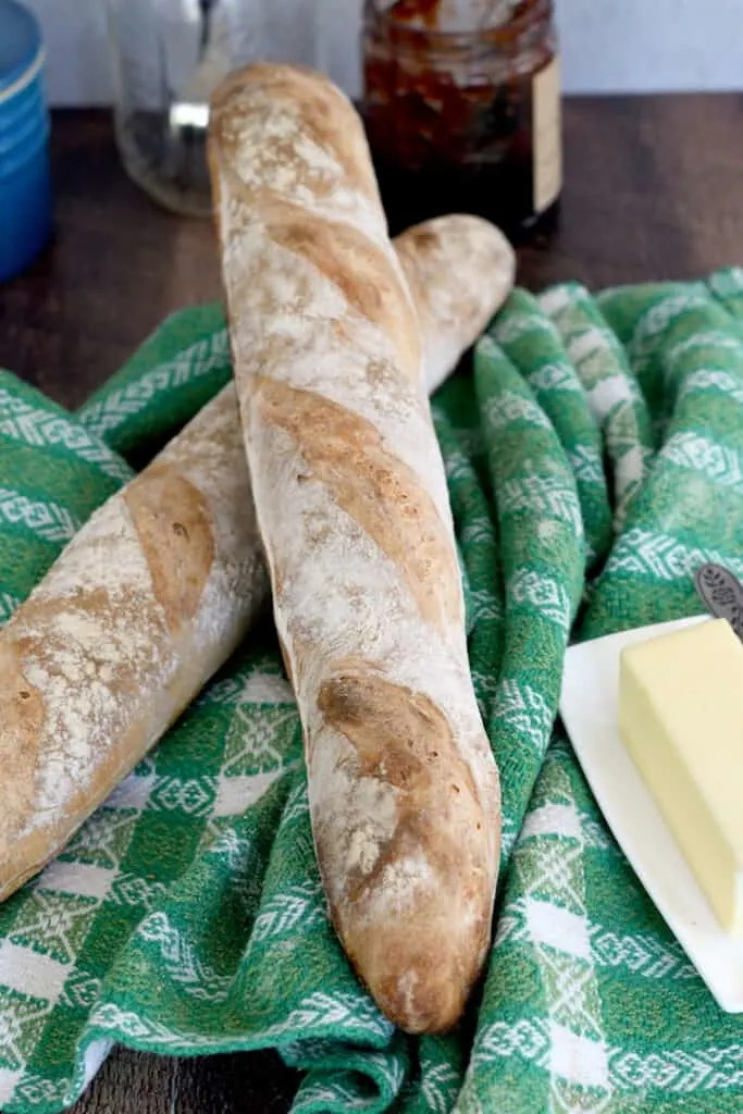 two sourdough baguettes on a green cloth with a stick of butter