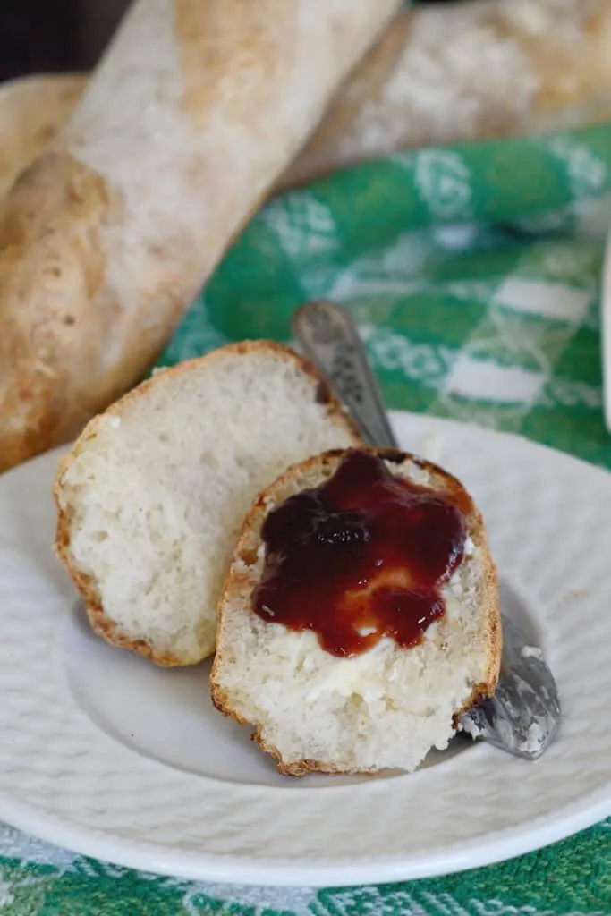 a piece of sourdough baguette on a white plate topped with butter and jam