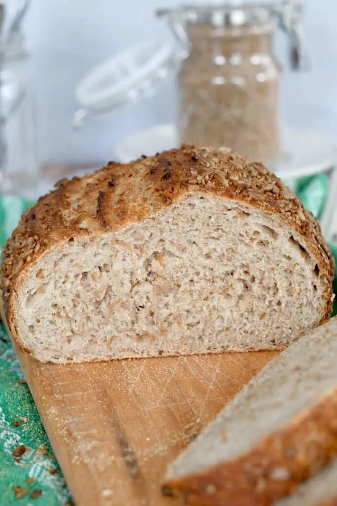 a sliced loaf of sourdough cracked wheat bread on a cutting board