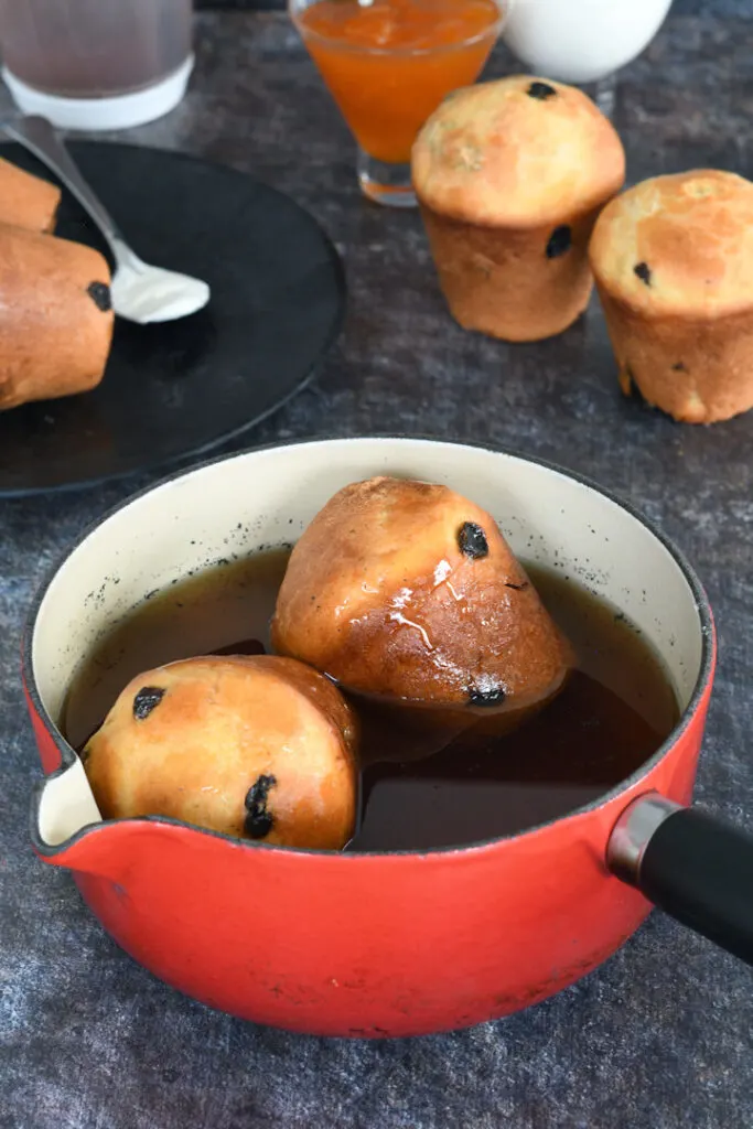 two sourdough babas soaking in rum syrup