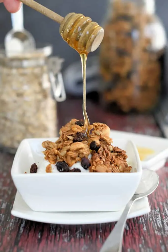 a bowl of yogurt topped with peanut butter granola with honey being drizzled on top