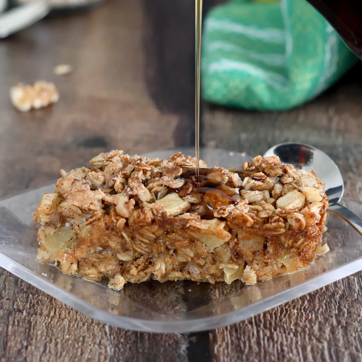 a slice of apple maple baked oatmeal on a plate being drizzled with maple syrup