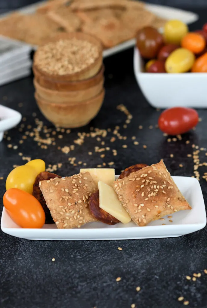 a plate with sourdough whole wheat crackers, cheese, sausage and tomatoes