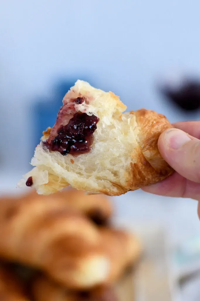 a hand holding a piece of croissant topped with fruit preserves
