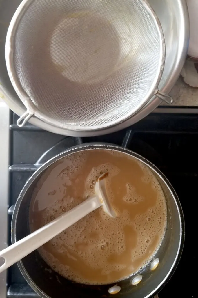 a pot of custard on a stove with a bowl and strainer nearby.