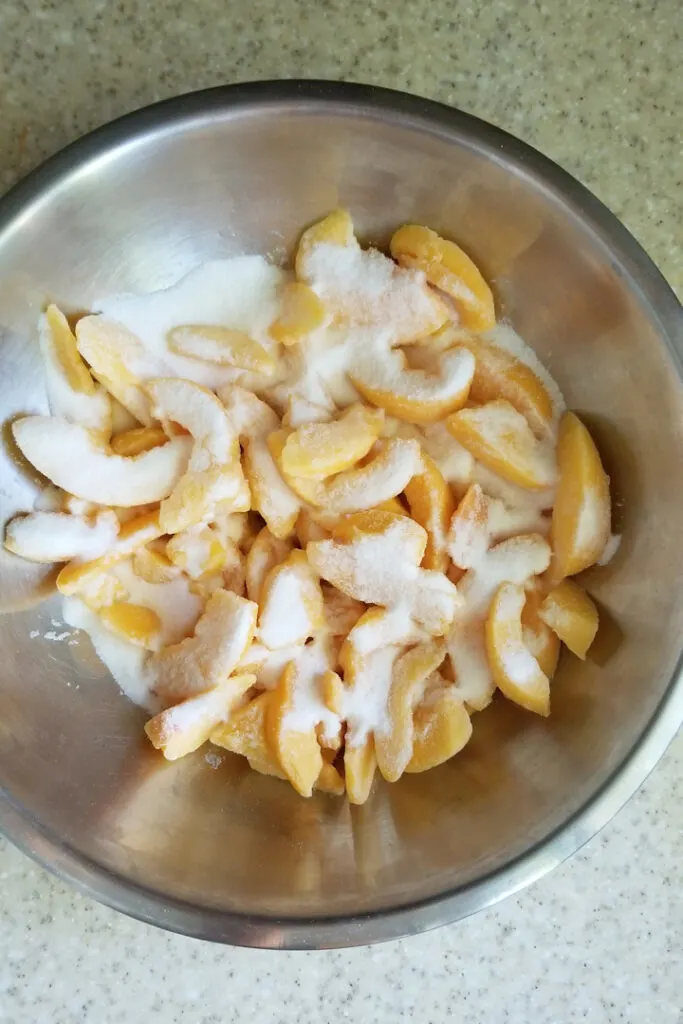 a mixing bowl filled with sliced peached sprinkled with sugar.