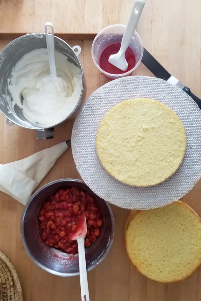 cake layers, white chocolate cream, cherry filling, a pastry bag, a spatula and cherry syrup on a work surface