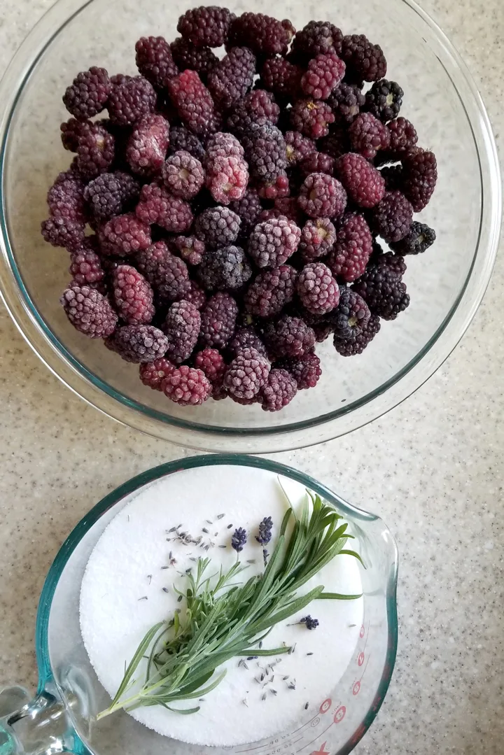 a bowl of blackberries and a bowl of sugar with lavender sprigs